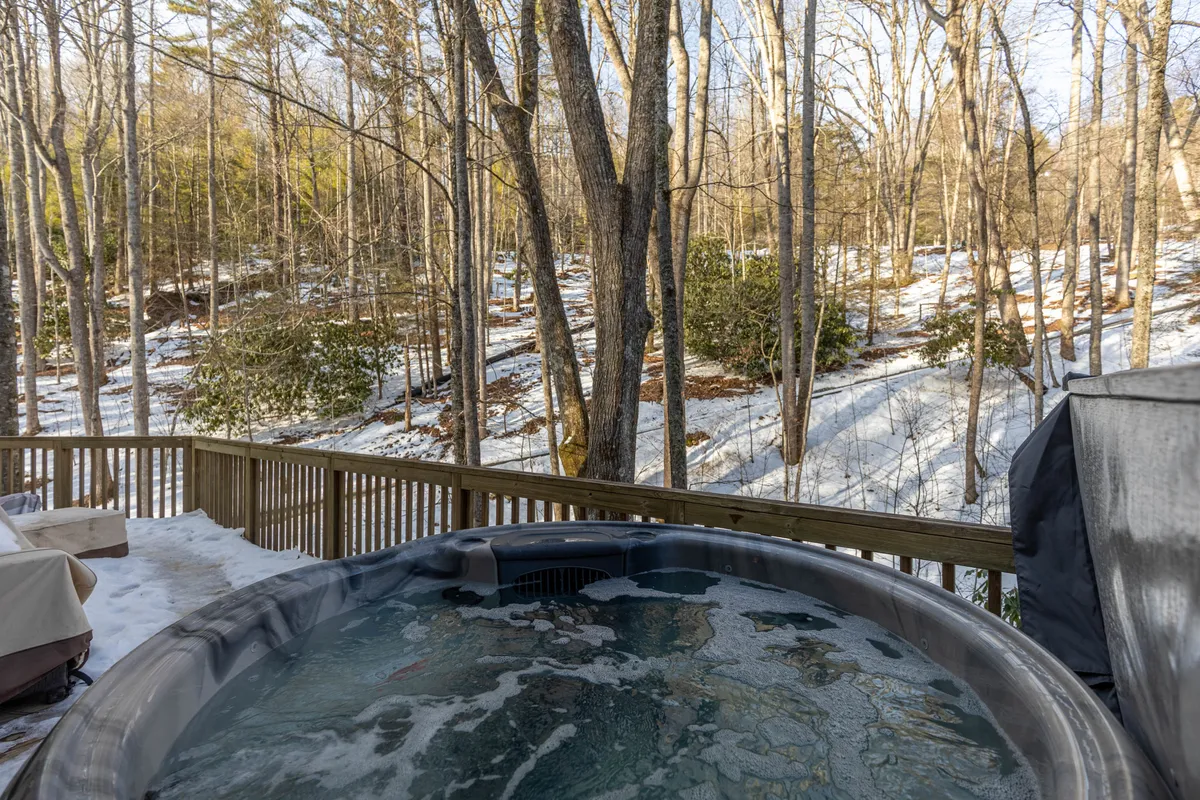 A steaming hot tub sits outdoors surrounded by snow-dusted trees, inviting relaxation even in winter. The scene is peaceful, highlighting the chalet's unique amenities and four-season appeal.