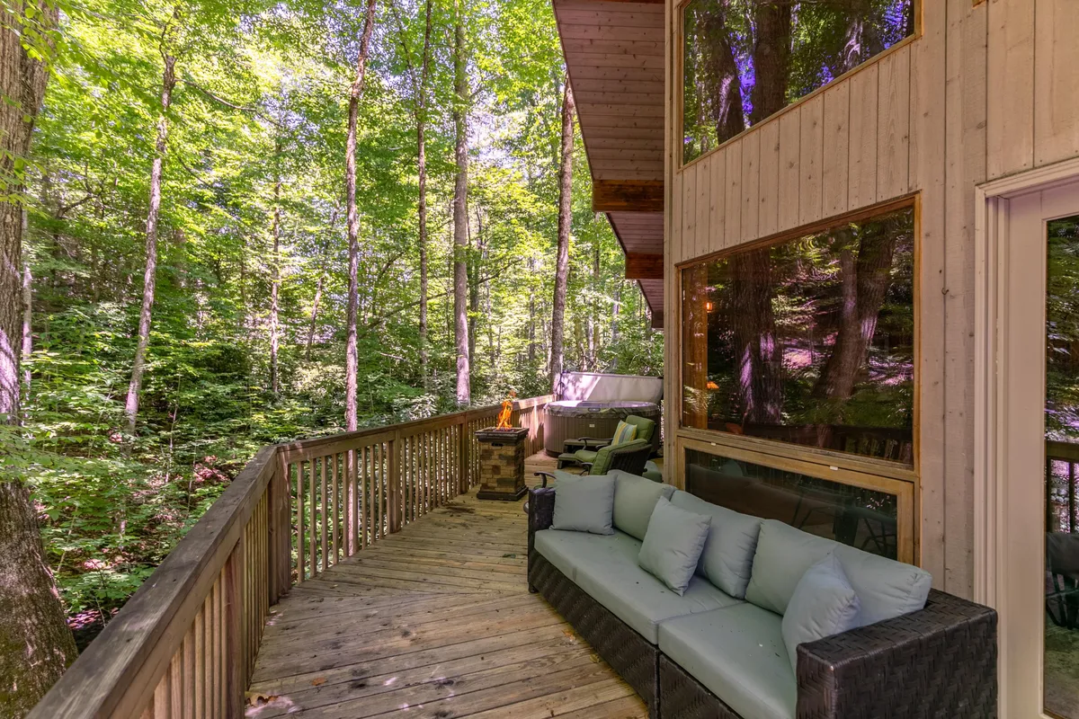 A peaceful outdoor deck scene with an inviting seating area and a fire pit, surrounded by lush green trees. The space is perfect for sipping drinks, sharing stories, and watching sunsets while being immersed in nature.