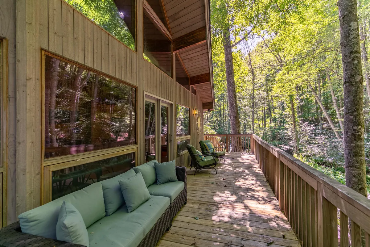 A peaceful wooden deck with green outdoor seating, large windows, and a backdrop of trees. The image emphasizes the connection between indoor comfort and the surrounding nature, with ample space for relaxation and play.
